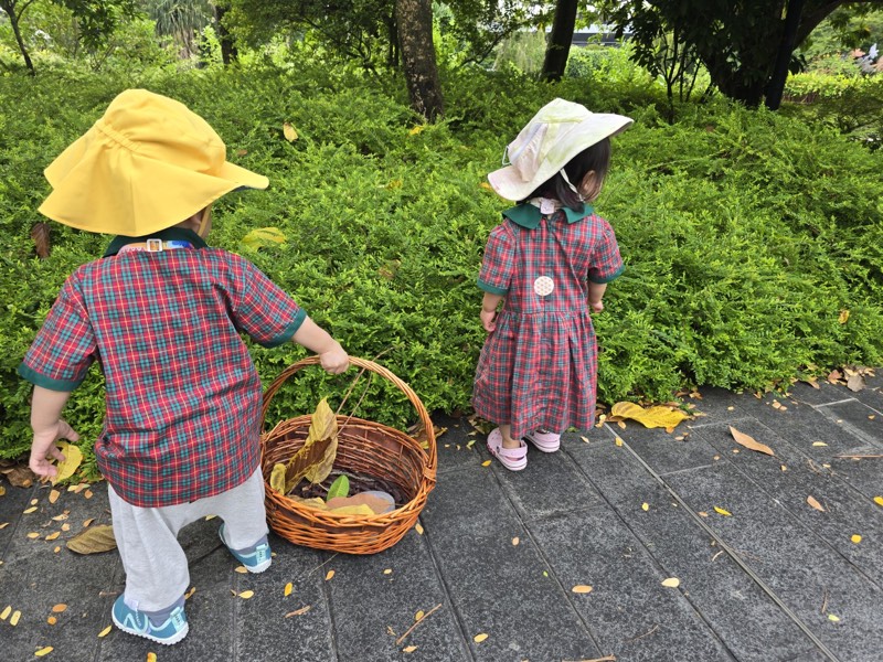 Two Pre-Nursery children gathering natural materials outdoors