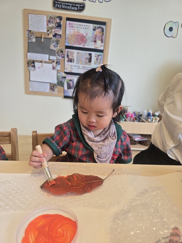 A Pre-Nursery child painting a leaf orange-red